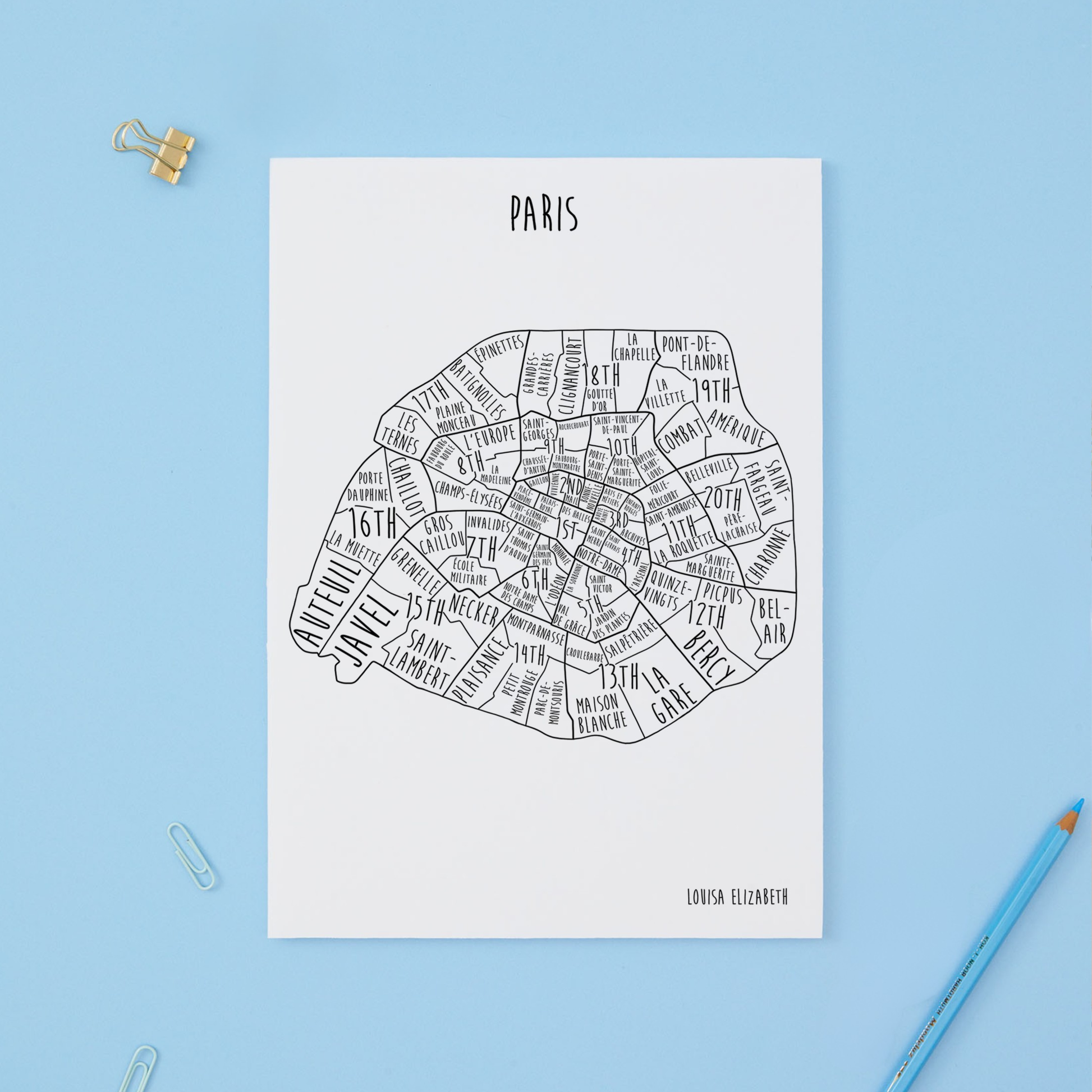 Map of Paris with neighborhood names on a white background, placed on a blue surface with a pencil and paper clips.